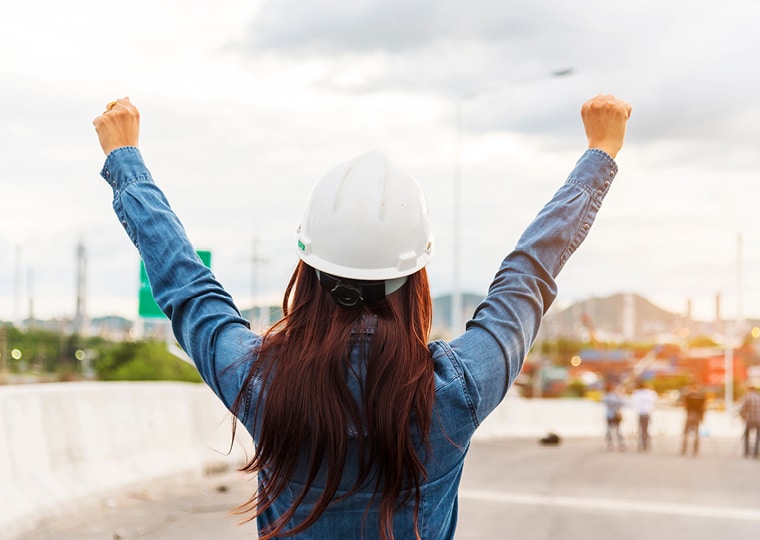 Woman in construction with hands raised in celebration